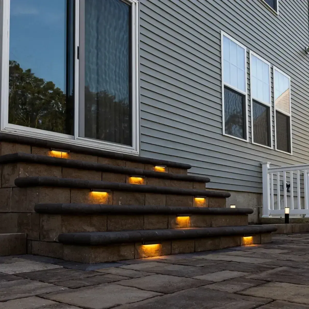 Wide paver steps with integrated step lights leading from a home to a patio