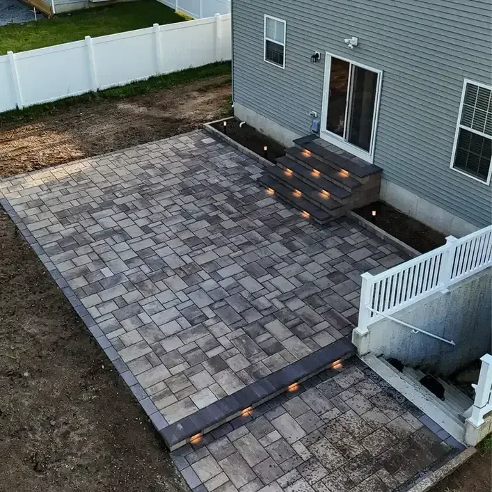 Paver patio with lit steps beside a deck