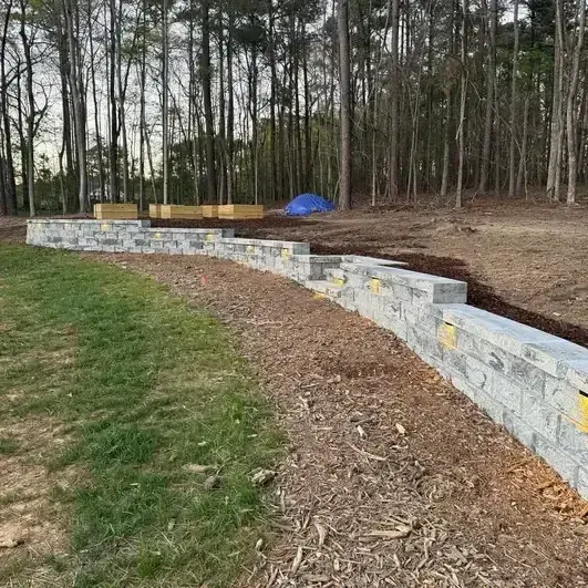 Segmental block retaining wall being built along a sloped wooded yard
